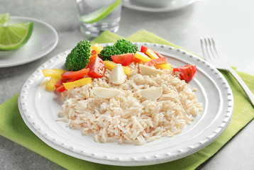 Plate with delicious brown rice and vegetables on table