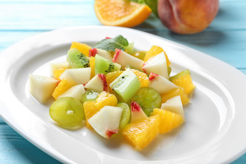 Plate with delicious fruit salad on wooden background