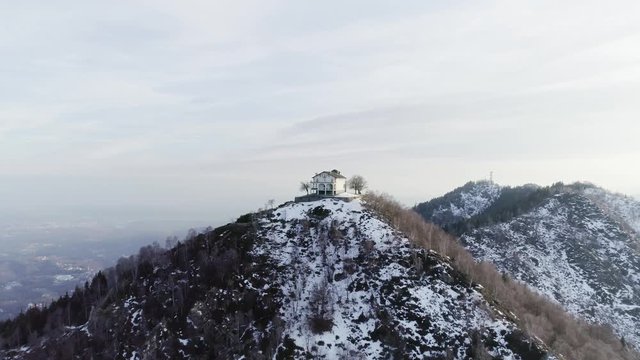 moving forward to building or church over the top of snowy mountain in autumn or winter at sunset.Pine woods forest and outdoor snow mountains aerial establisher.4k drone flight establishing shot