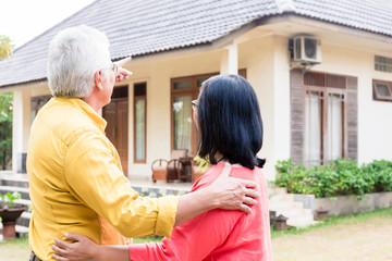 Elderly man pointing to a comfortable residential house while standing close to his wife