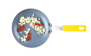 Frying pan with cooking oil, chopped garlic and chili on white background