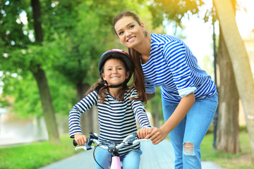 Obraz premium Mother teaching her daughter to ride bicycle in park on sunny day