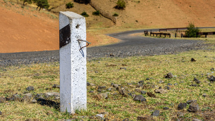 White concrete road column with black diagonal stripe staying on the side of the serpentine road with stones on the ground