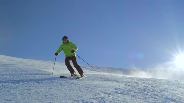 SLOW MOTION FOLLOW Amateur skier skiing for recreation in perfect early morning snowy winter day on a fresh groomed piste at the modern European ski resort. Sun is shinning above the fog.