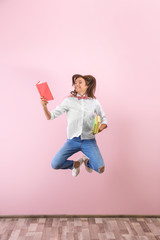 Jumping teenager girl with books near color wall