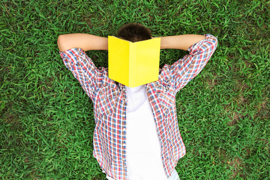 Teenager boy with book lying on green grass