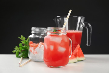 Jug and mason jars with watermelon juice on table against black background