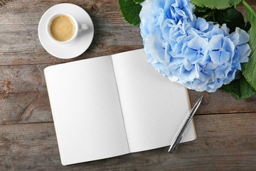 Composition with beautiful blue flowers, notebook and cup of coffee on wooden background