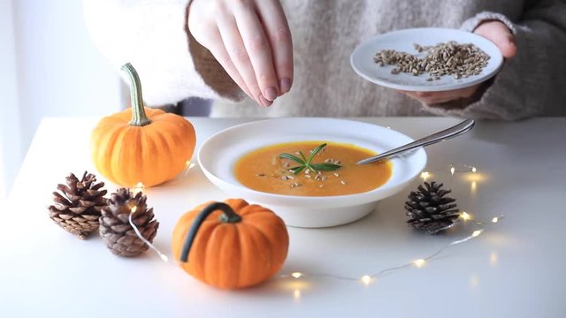 Pumpkin soup with rosemary in white plate near a pine cone with Fairy Ligths