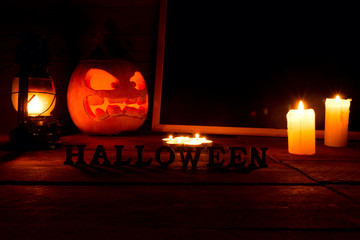 The concept of Halloween. Glowing with a fiery yellow light, an evil, terrible pumpkin with candles and a chalkboard. mystical jack lantern in the dark, on a wooden background with text Halloween