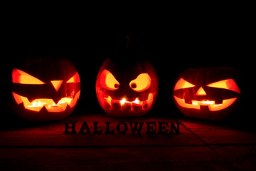 The concept of Halloween. A lot of Evil scary pumpkin in the dark. Jack Lantern in the darkness with Halloween inscription