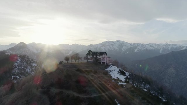 orbit around building or church over the top of snowy mountain in autumn or winter at sunset.Pine woods forest and outdoor snow mountains aerial establisher.4k drone flight establishing shot