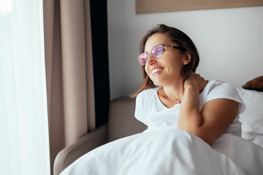Happy smiling woman in eyeglasses meets new day in bedroom