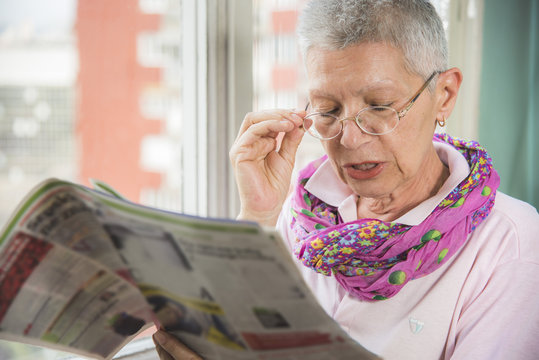Senior elderly lady having troubles with her eye glasses, can't see well and can't read the small letters in the newspapers