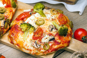 Tasty Italian homemade mini pizzas with broccoli, feta and olives served on wooden cutting board.