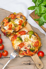 Tasty Italian homemade mini pizzas with broccoli, feta and olives served on wooden cutting board.
