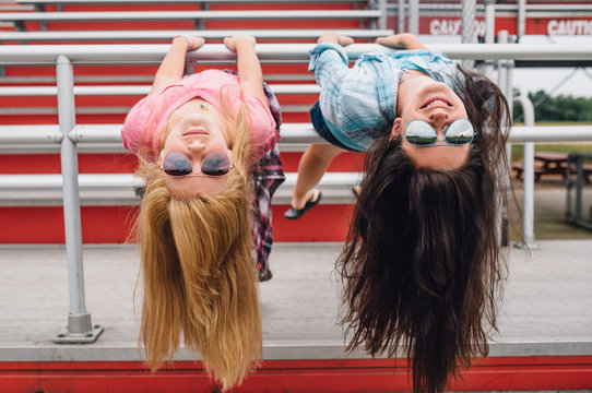 Two girls hanging upside down at bleachers