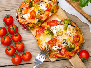 Tasty Italian homemade mini pizzas with broccoli, feta and olives served on wooden cutting board.