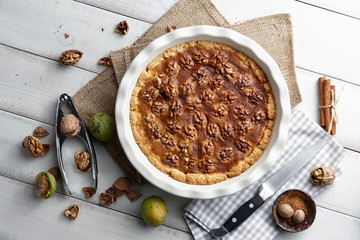 Traditional walnut pie with nuts and nutcracker on white wooden planks, top view