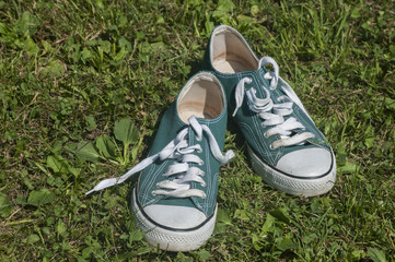 Old used weathered green sneakers closeup on grass background