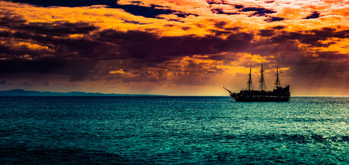 A lone ship against the morning sky. A distant historic ship in dramatic atmosphere.