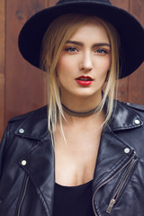 Close up of most beautiful young woman with gorgeous long blonde hair is looking at you. Wearing leather jacket, fashionable black hat and choker around neck.