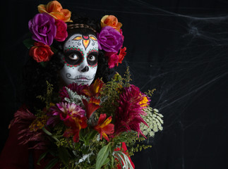 Little girl Halloween costume and makeup of La Calavera Catrina. Portrait of a little girl with white painted face and bouquet of flowers. Day of the dead