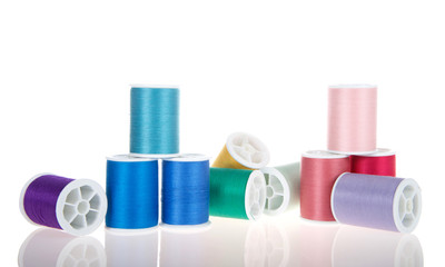 Many spools of sewing thread stacked and on side isolated on white on a reflective surface haphazardly laying and stacked
