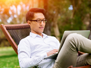 Fototapeta premium Young businessman using laptop while sitting outdoors