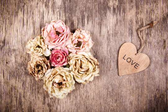 Dry roses and a wooden heart. Romantic concept. Dried flowers on a wooden background.