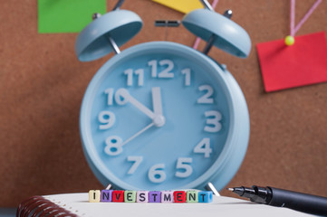 Close up shot of the colorful alphabet beads forming word Investment with alarm clock on the background.