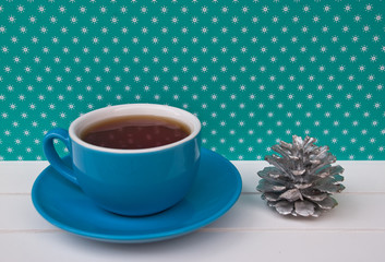 Blue Cup of tea on green background with white snowflakes and small decor silver pine. Beautiful color. New Year still life.