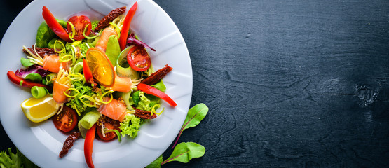 Salad with salmon and fresh vegetables and herbs. Italian cuisine. Top view. On Wooden background.