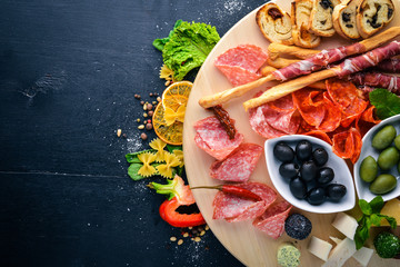 Cold snacks. Chopped sausage, bacon, olives, olives. Top view. Wooden background. Free space for text.