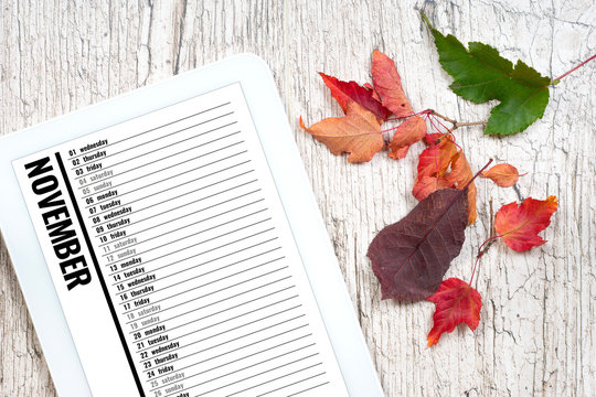 november calendar in electronic organizer on wooden textured table with colorful autumn leaves