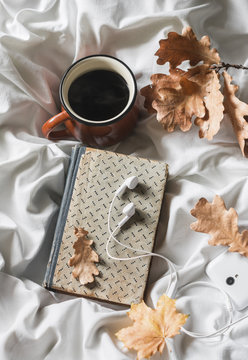 Coffee, book, headphones, phone on the bed, top view. Leisure, cozy home concept. Warm autumn mood
