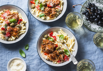 Italian food table. Pasta with slow cooker chicken with olives and sweet peppers, white wine. On a blue background, top view