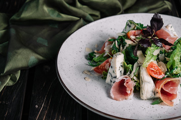 Green salad with prosciutto and blue cheese served with fabric on dark wooden background
