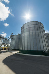 Fototapeta na wymiar High metal silos for storage of wheat and barley. Sunny day, the blue sky.