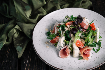 Green salad with prosciutto and blue cheese served with fabric on dark wooden background
