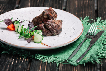 Grilled beef steak served with green napkin and cutlery on dark wooden background