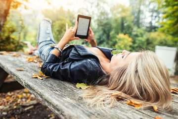 Blonde girl read ebook lying on wooden table in autumn park