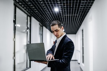 Fototapeta premium Handsome young man holding laptop in office