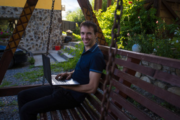 Young man sitting outdoor in front of blue sky with laptop and working 