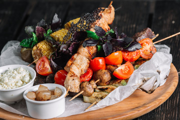 Fototapeta na wymiar Assorted delicious grilled meat with vegetable served with cracklings and brynza on a wooden board on dark wood background