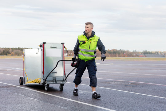 Worker Pulling Machine On Cart At Airport Runway