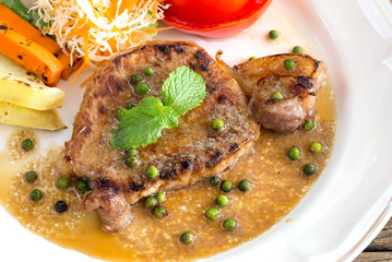 Pork steak and vegetables with salad dressing in white dish on old wooden table ..