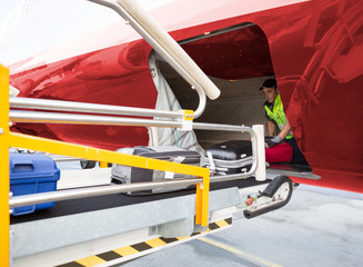 Worker Placing Baggage On Conveyor While Unloading Airplane
