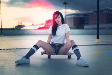 Trendy young woman sitting on skateboard in sunset © sakkmesterke