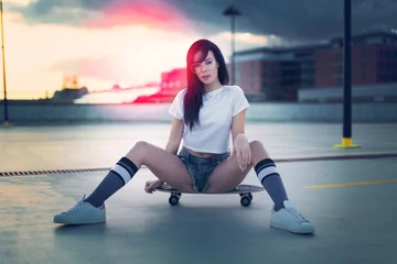 Foto op Plexiglas Trendy young woman sitting on skateboard in sunset © sakkmesterke